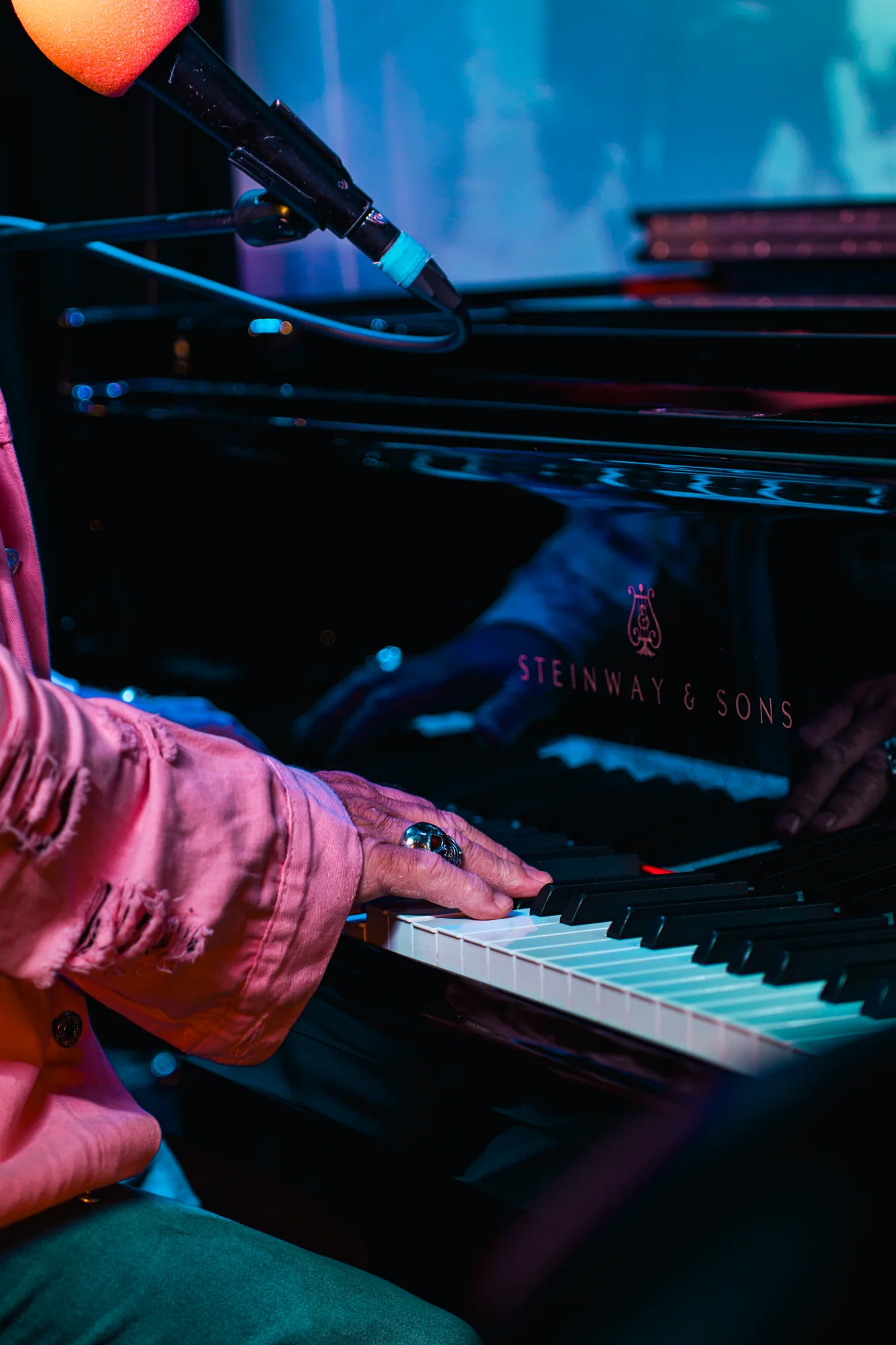 Musician playing a Steinway piano under blue stage lighting
